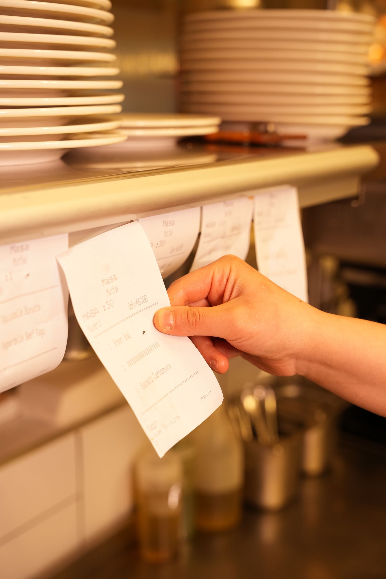 A hand pulling one paper order from a crowded restaurant kitchen ticket rail